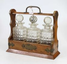 An Edwardian brass mounted oak three bottle tantalus, surmounted by a carrying handle, containing