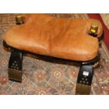 An ebonised, brass mounted and further studded camel stool, with tan leather cushion seat