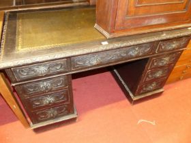 A circa 1900 ebonised and heavily relief carved oak twin pedestal writing desk, having a gilt tooled