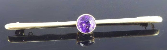 A yellow metal amethyst bar brooch, having a centre round amethyst in a bezel setting, amethyst