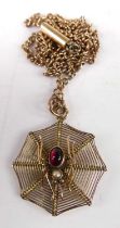 A 9ct gold pendant fashioned as a spider web, the spider set with a cabochon ruby and seed pearl, on