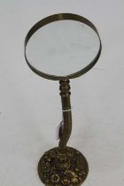 An early 20th century brass adjustable desk magnifying glass, the base relief decorated with