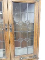 An Arts & Crafts oak and copper mounted bookcase over desk, having twin lead glazed upper doors, the