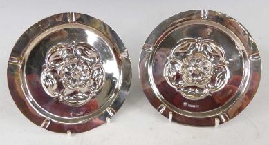 A pair of circa 1900 silver circular ashtrays, each with embossed rose head to centre, maker