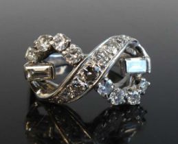 A white metal diamond crossover ring comprising 17 graduated round brilliant and 2 baguette cut