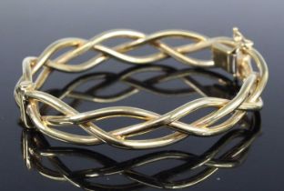 A contemporary 9ct gold hinge bangle arranged as three interwoven bands, with safety chain, 18.9g,