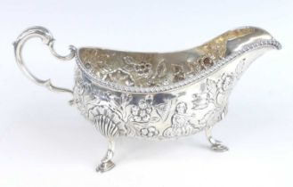 A late Victorian silver sauceboat, having all-over repousse decoration depicting two seated