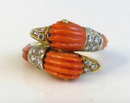 A yellow metal and coral and diamond twin duck head crossover style ring featuring carved coral