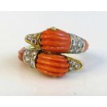 A yellow metal and coral and diamond twin duck head crossover style ring featuring carved coral