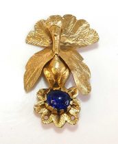 A gilt metal engraved peacock brooch surmounting a 12 by 10mm oval blue paste cabochon stone in an
