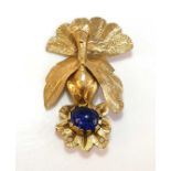 A gilt metal engraved peacock brooch surmounting a 12 by 10mm oval blue paste cabochon stone in an