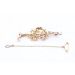 An Edwardian 15 ct yellow metal bar brooch, having a horseshoe, entwined by ivy, on a riding crop,