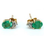 A pair of modern emerald and diamond stud earrings, each having an oval emerald claw set below a