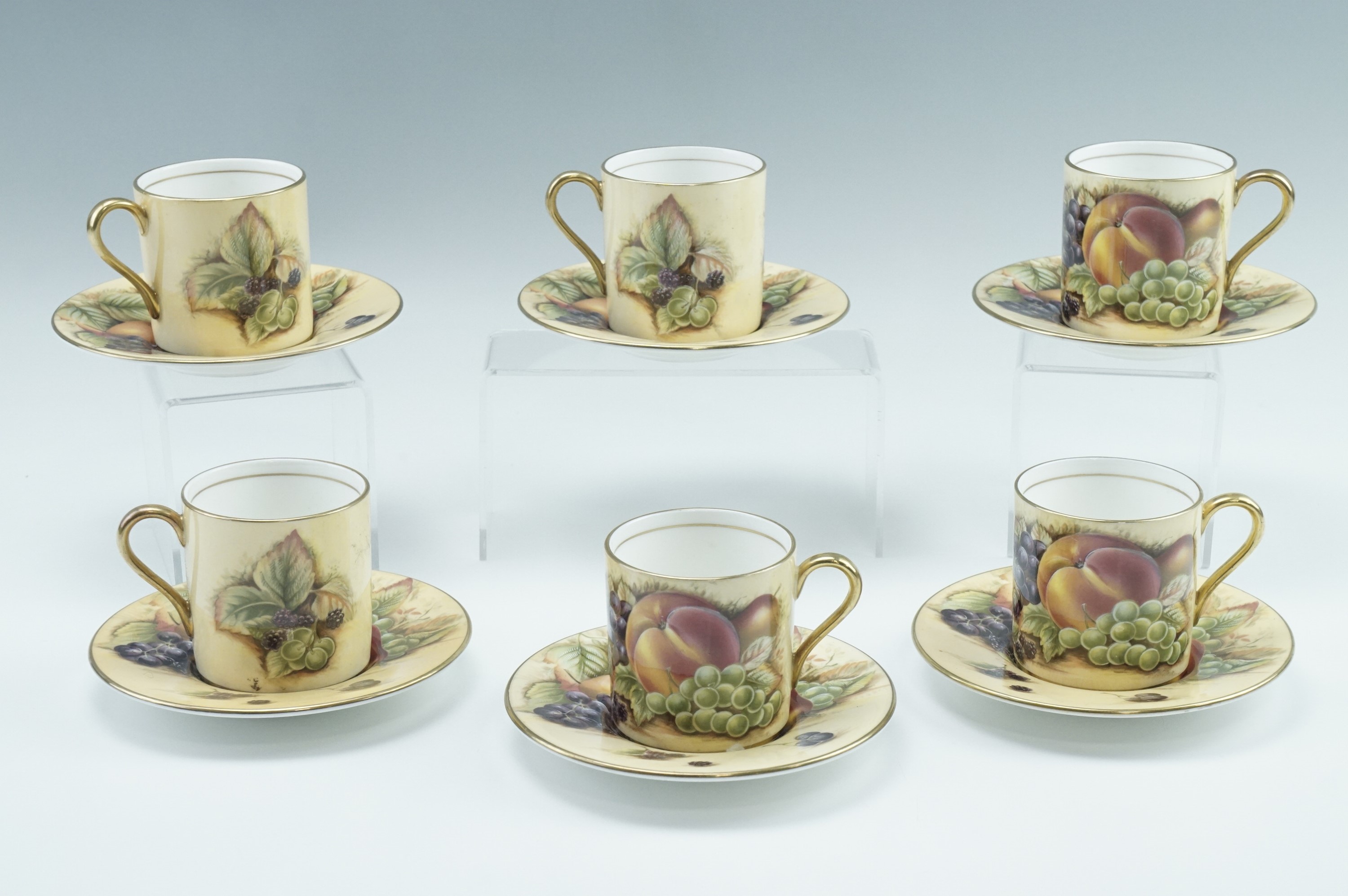 Six Aynsley Orchard Gold coffee cans and saucers, transfer decorated with fruit, late 20th