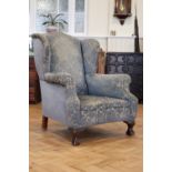 A late 19th / early 20th Century upholstered wing-back lounge armchair, having carved claw-and-