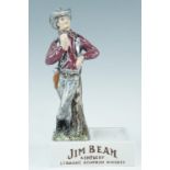 A Jim Beam ceramic counter top figural display stand, modelled as a cowboy sipping a bourbon, the