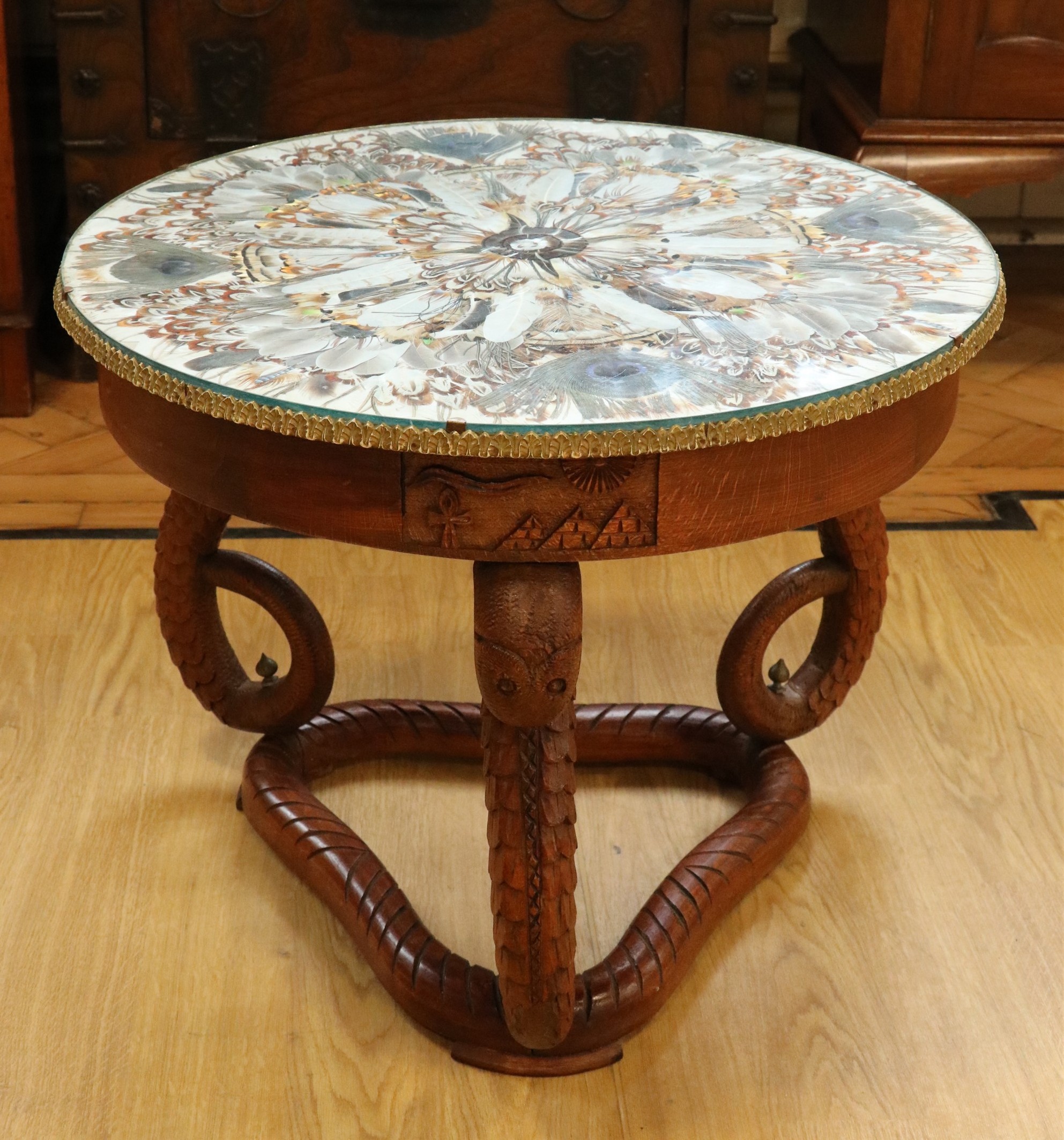 An Egyptian carved hardwood coffee table, having serpent-form legs and a glass and peacock feather