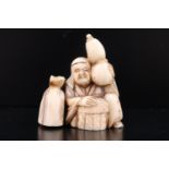 A Meiji Japanese carved marine ivory netsuke modelled as a hooded figure sat holding a double