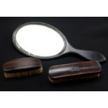 Two ebony handled brushes together with a hand mirror, mirror 33.5 cm overall