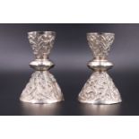 A pair of Indian white metal candlesticks, bearing embossed foliate scroll and figural decoration,