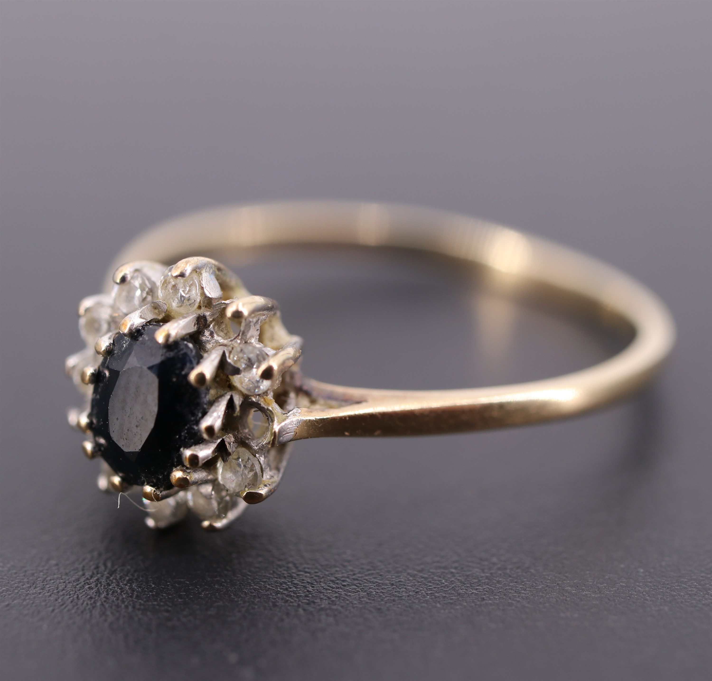 A sapphire, white paste and 9 ct gold flowerhead cluster ring, the oval sapphire of approx 0.3 ct,