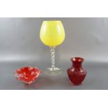 A large free blown wine glass, having a yellow bowl and spiral stem, together with a red glass