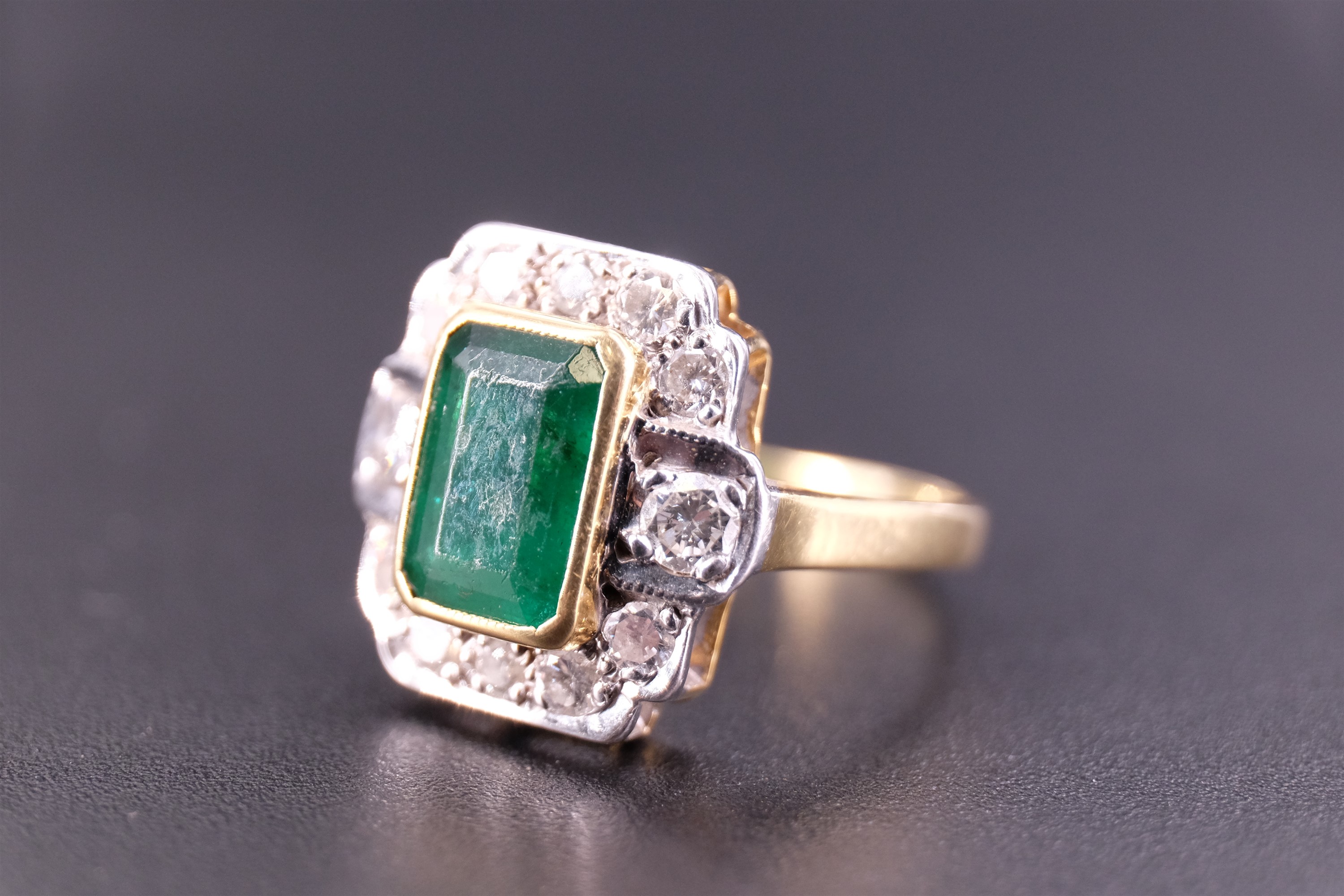 An Art Deco emerald and diamond ring, the central 'emerald' cut 1.75 carat emerald set in a yellow