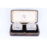 A cased pair of 1920s silver napkin rings, each of oval section and decorated with engine-turned