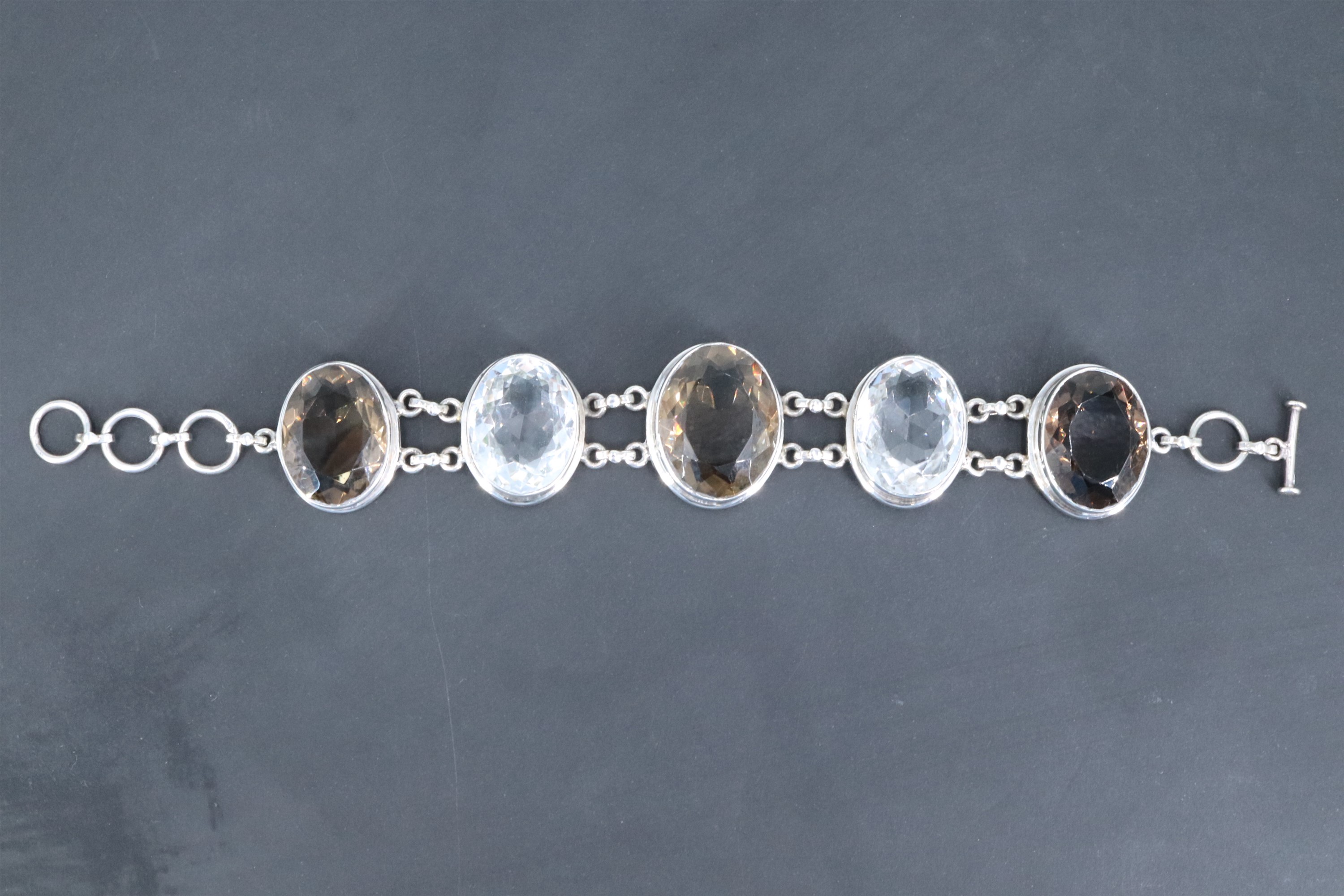 A contemporary white metal bracelet of large facet-cut oval smoky quartz and rock crystal jewels,