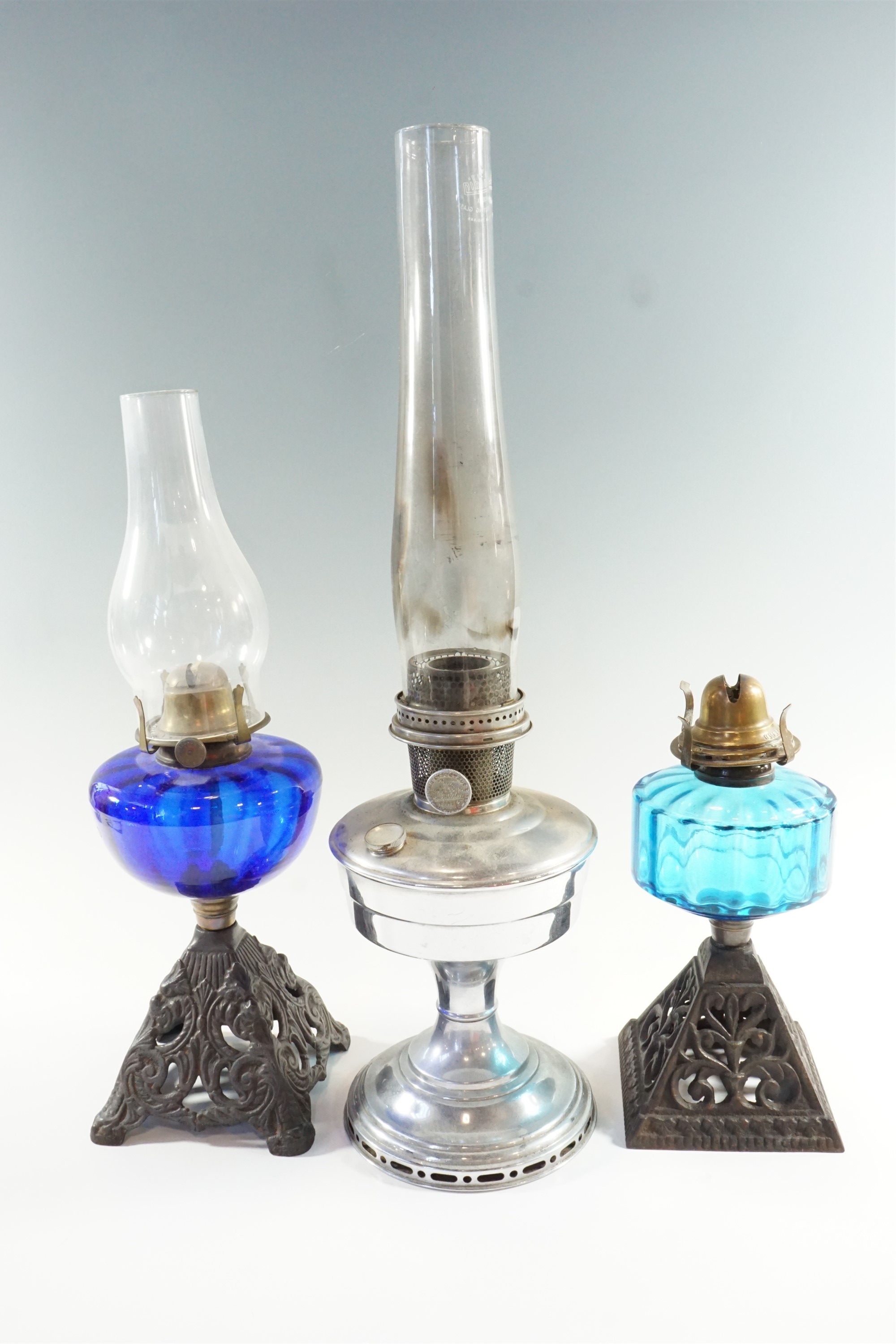 Two early 20th Century cast iron and blue glass oil lamps, both having single wick prong burners,