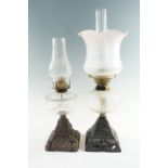 Two 20th Century cast iron and glass oil lamps, respectively having a moulded glass font, a duplex