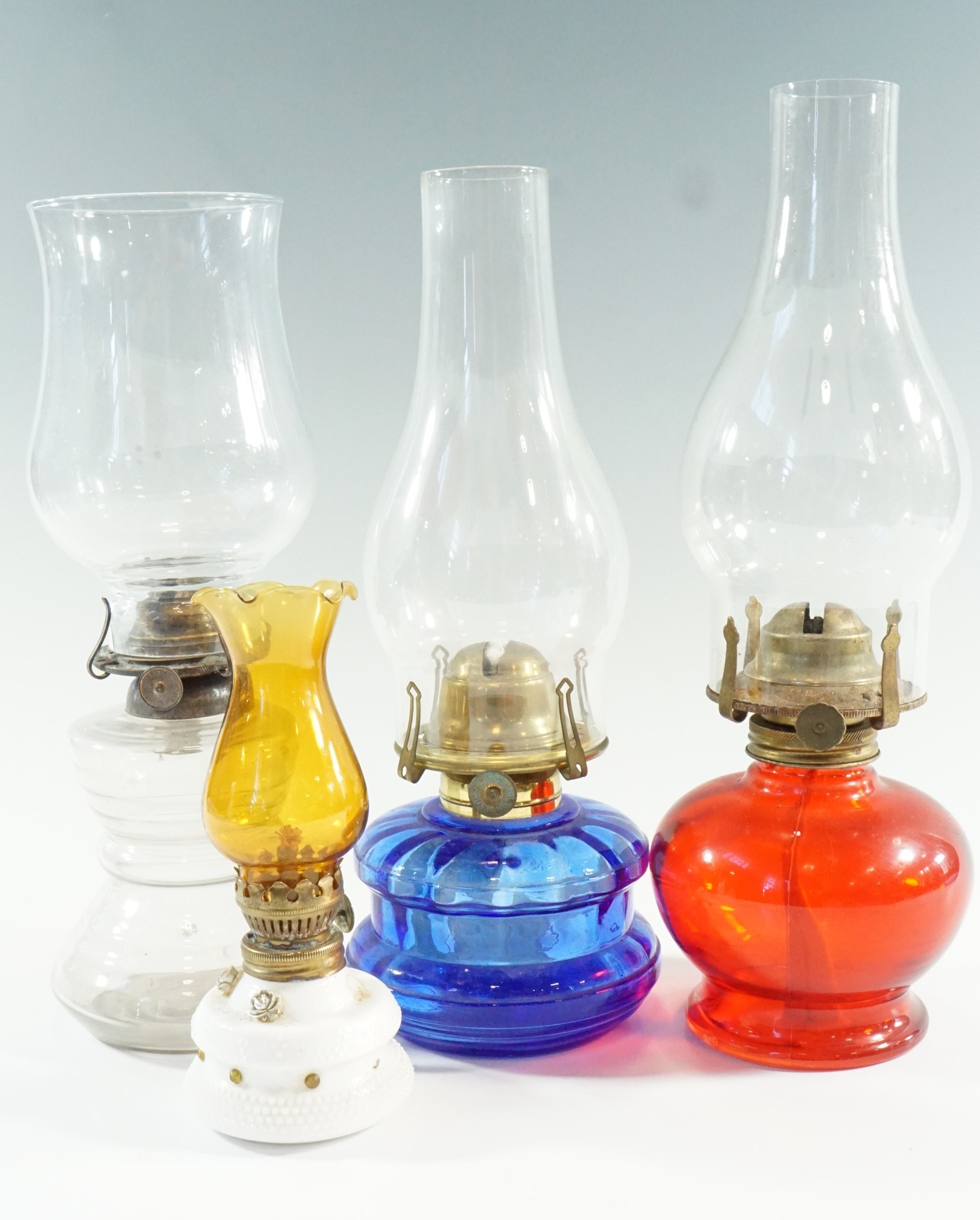Three early 20th Century bedroom oil lamps, comprising moulded ruby and blue glass, and a clear