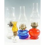 Three early 20th Century bedroom oil lamps, comprising moulded ruby and blue glass, and a clear