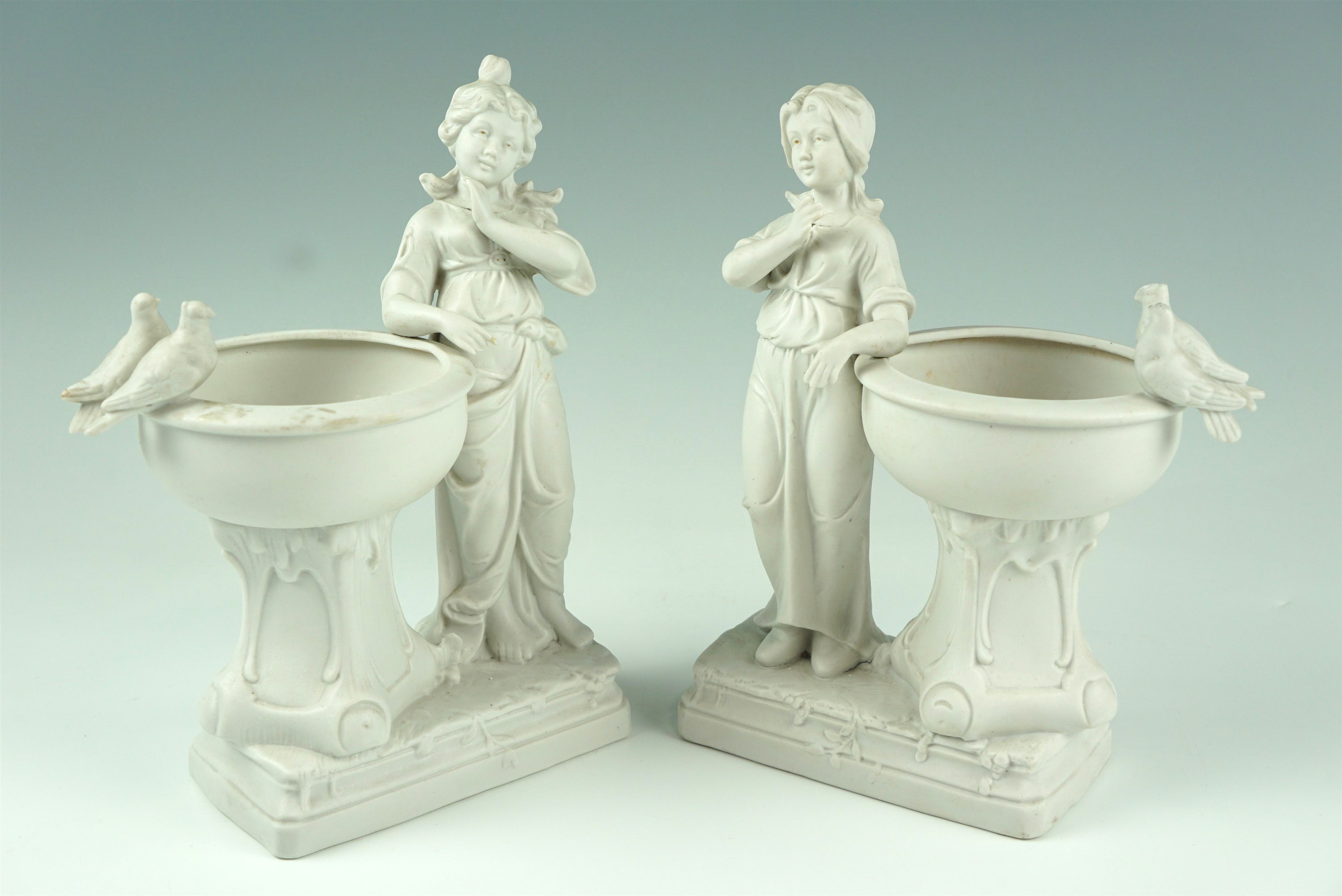 A pair of late 19th / early 20th Century bisque figural vases, modelled as children beside urns,