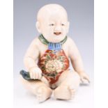 An early 20th Century Japanese ceramic figurine of a seated child, 20 cm