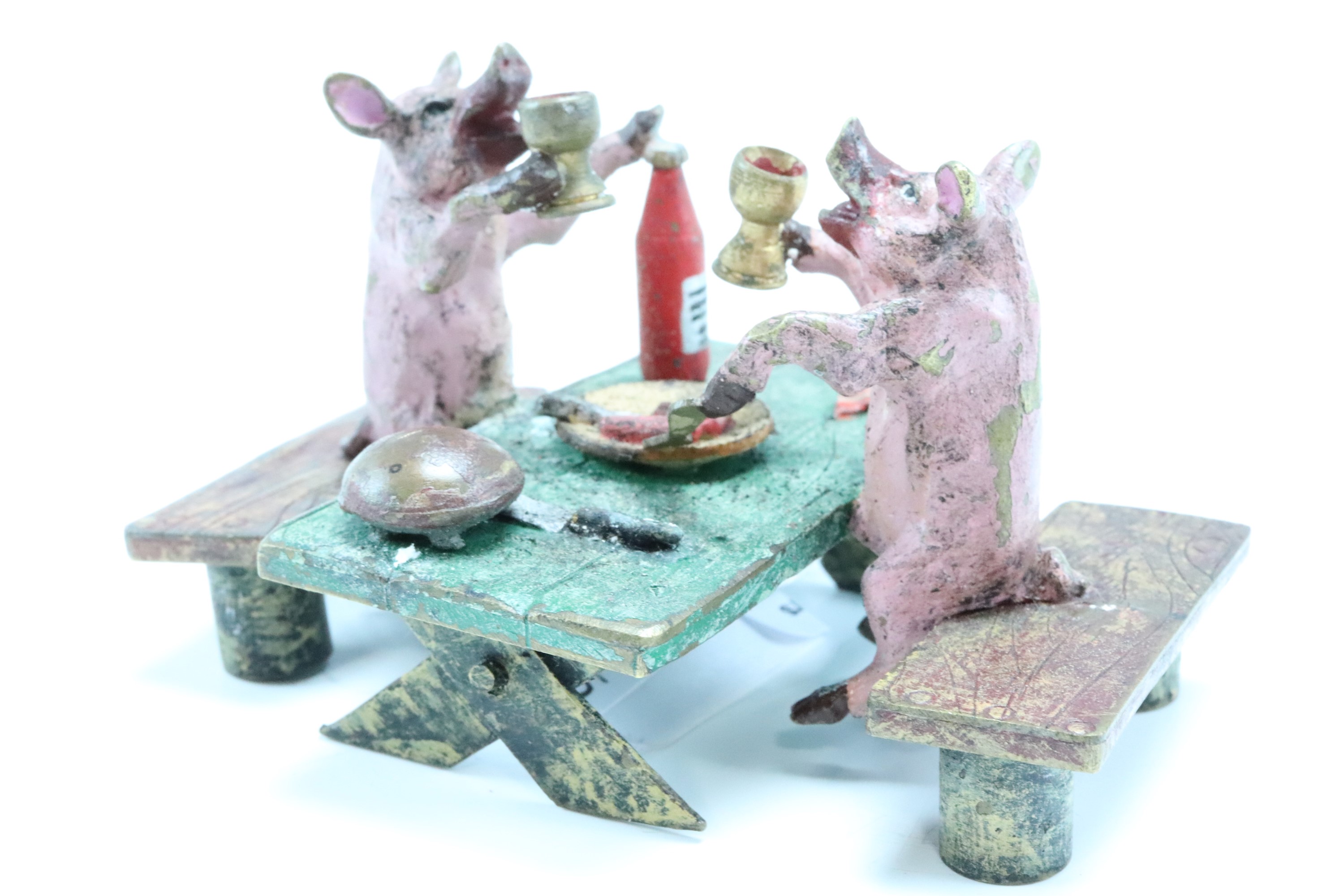 A cold painted bronze figure of two pigs at a picnic table quaffing wine, impressed mark to base,