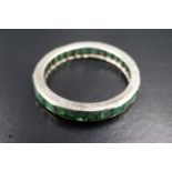An emerald and precious white metal eternity ring, the square-cut stones channel-set and of 1.24