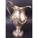 A Victorian silver milk jug, of helmet form raised on a foot and having repoussé and applied cast