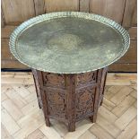 A Middle Eastern brass tray top table decorated with Egyptian motifs and having a carved folding