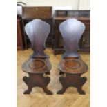 A pair of George III mahogany hall chairs of sgabello form, the seat being subtly dished, the shaped