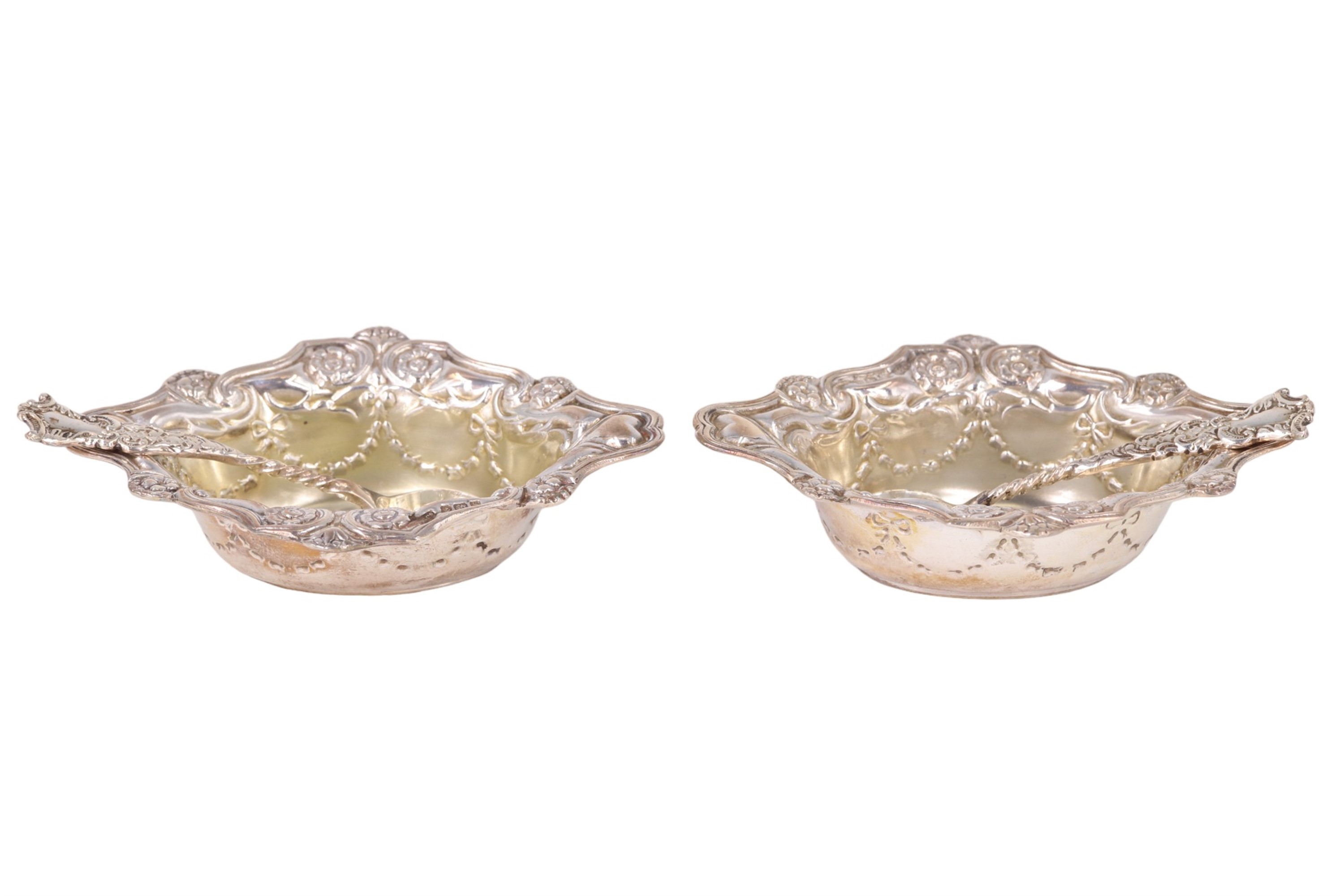 A cased pair of Edwardian silver salt cellars, having embossed decoration, associated spoons,