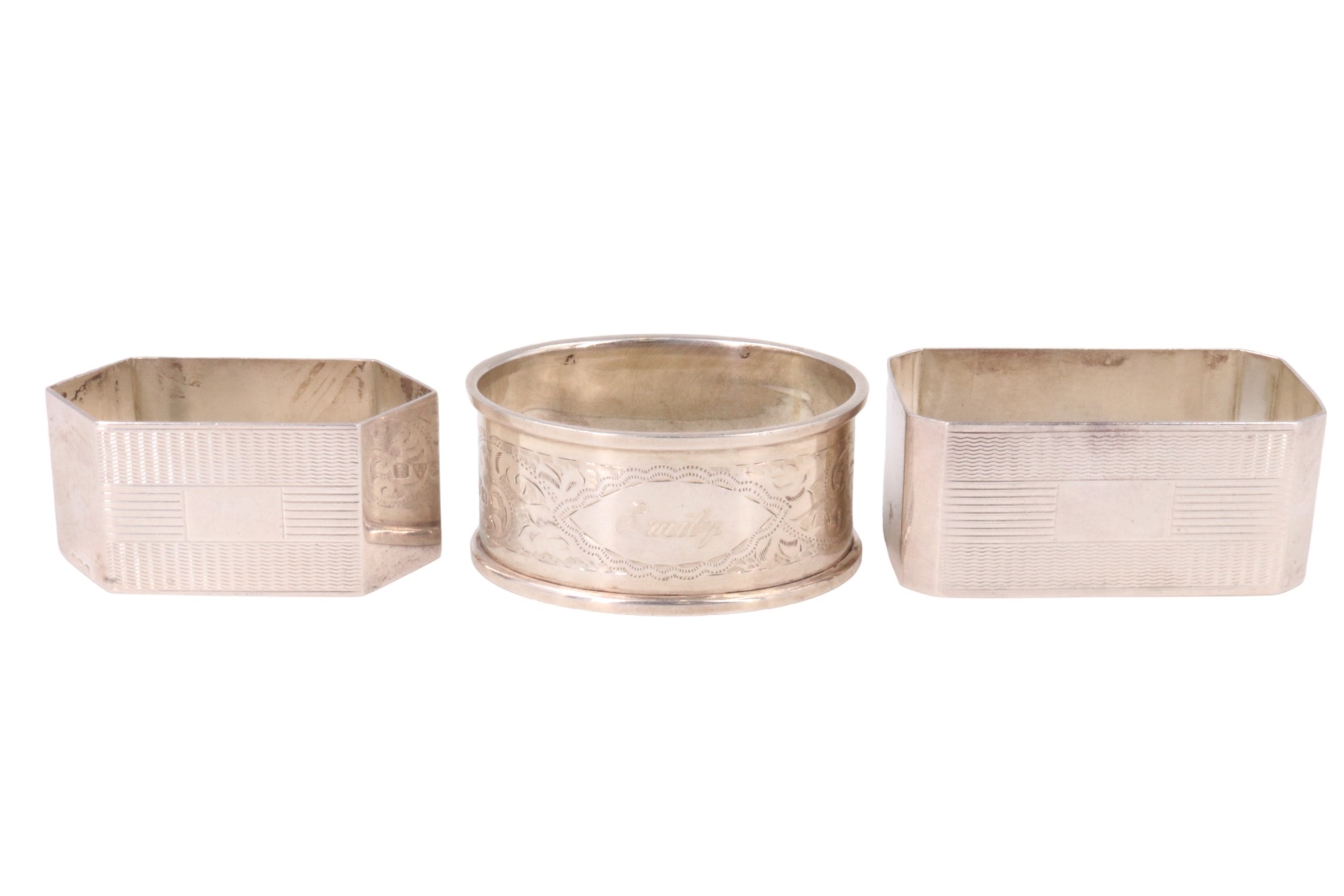 Three silver napkin rings, comprising two engine turned with vacant cartouches, and one floral