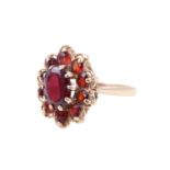 A 1970s garnet daisy ring, comprising a central claw-set oval cut garnet of 6 mm x 8 mm,