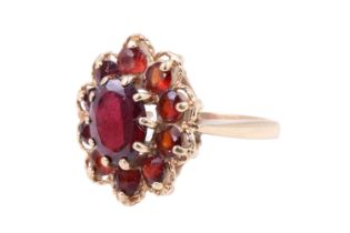 A 1970s garnet daisy ring, comprising a central claw-set oval cut garnet of 6 mm x 8 mm,