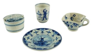 Four items of Delft blue-and-white ceramics, comprising a beaker, a square mug, a saucer, and a