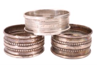 Three George V silver napkin rings, comprising a pair having embossed beaded decoration and one with