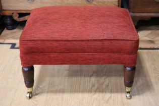 A contemporary upholstered footstool, having turned legs and brass cups and casters, 59 x 43 x 40