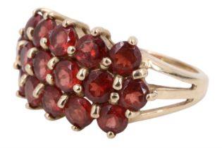 A contemporary Mozambique garnet cluster set ring, having a line of six 3.5 mm brilliants, nestled