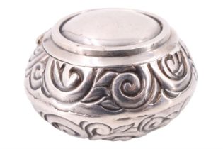 A 1920s silver and gilt lined pill box, having scrolled repoussé decoration and a hinged lid,