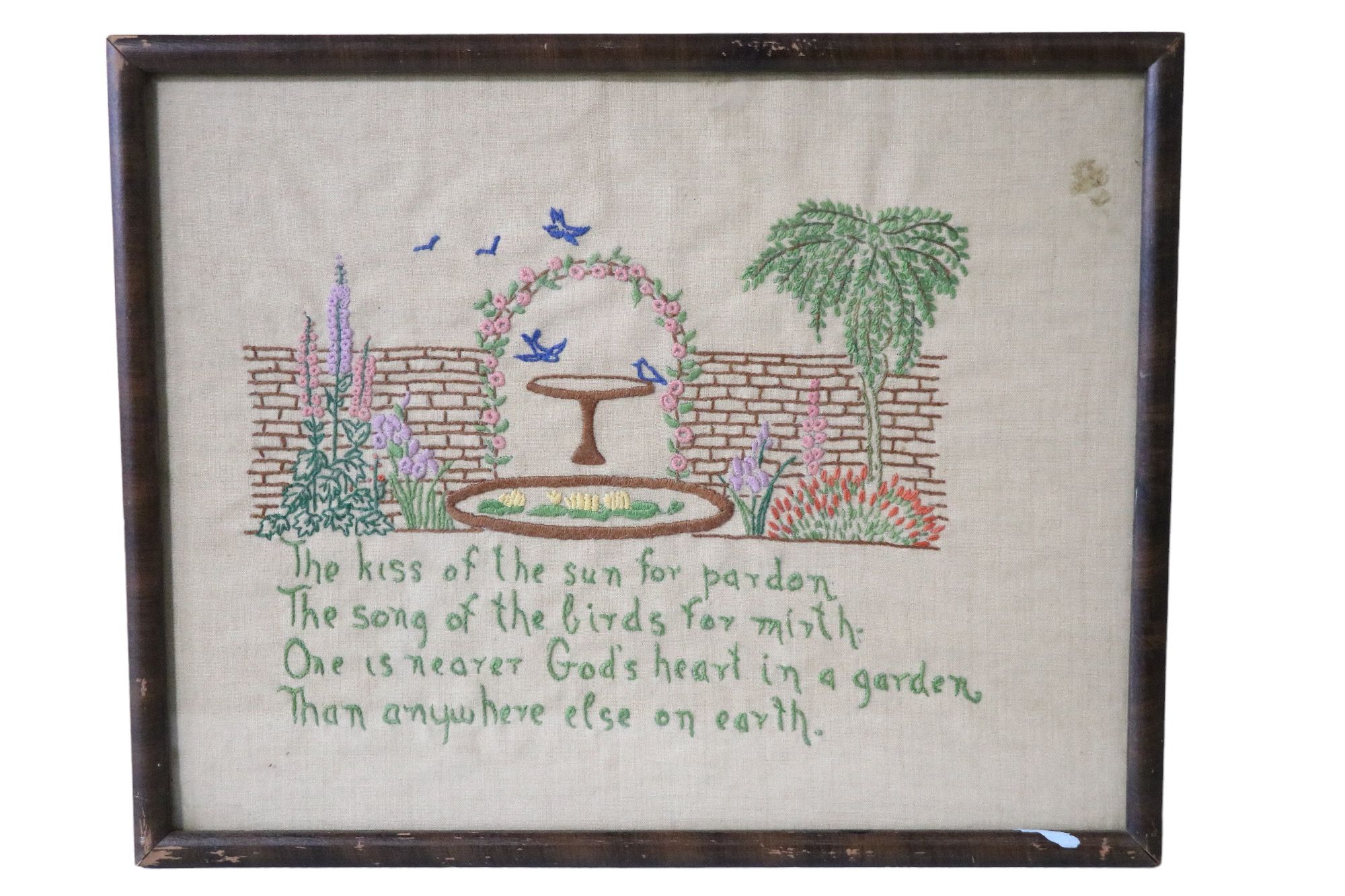 A religious text embroidered in depiction of a walled garden with a lily covered pond and birds